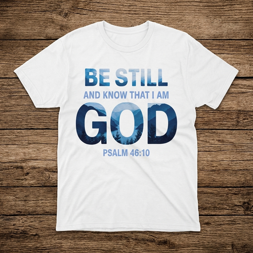 White t-shirt with 'Be Still and Know That I Am God' text on a wooden surface
