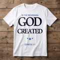 White t-shirt with 'In the Beginning God Created Genesis 1:1' text on a wooden background