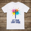 White t-shirt with colorful cross design and 'Let Your Light Shine' text on a wooden surface